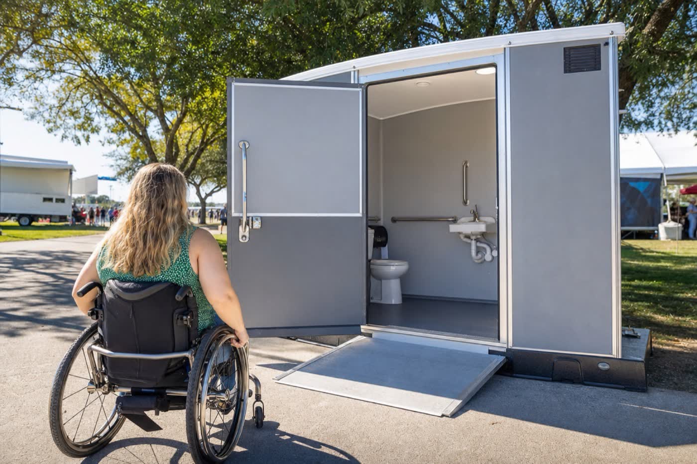 A wheelchair-accessible portable restroom with a ramp and grab bars at a park event